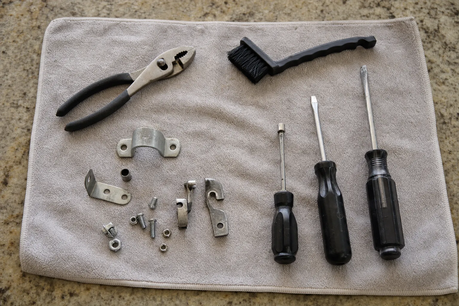 Pliers, a wire brush, nut driver and screwdrivers laid out with brackets and fasteners