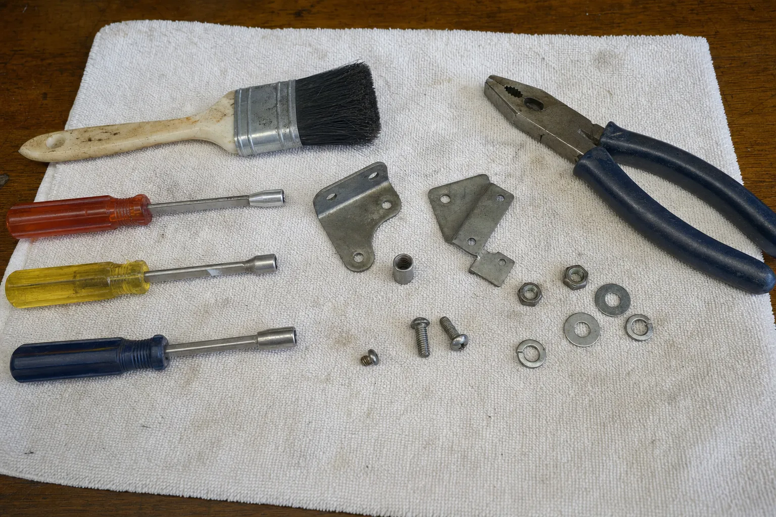 Nut drivers, pliers, a brush and two steel brackets with their bolts and washers on a cloth