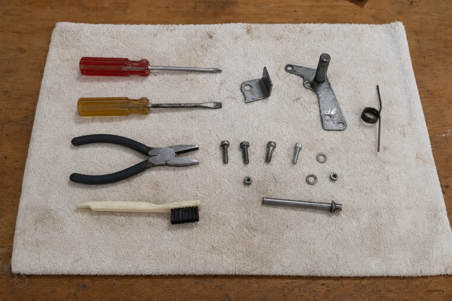 Screwdrivers, pliers and a wire brush beside a latch arm, spring and fasteners on a cloth